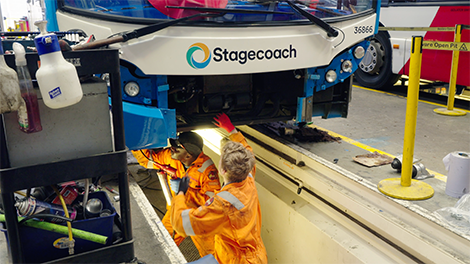 Engineers repairing a bus in a pit at a depot