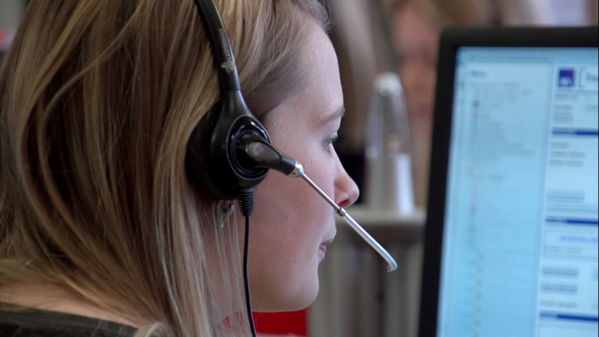 Person wearing a headset looking at a computer monitor in a busy AXA Health call‑centre