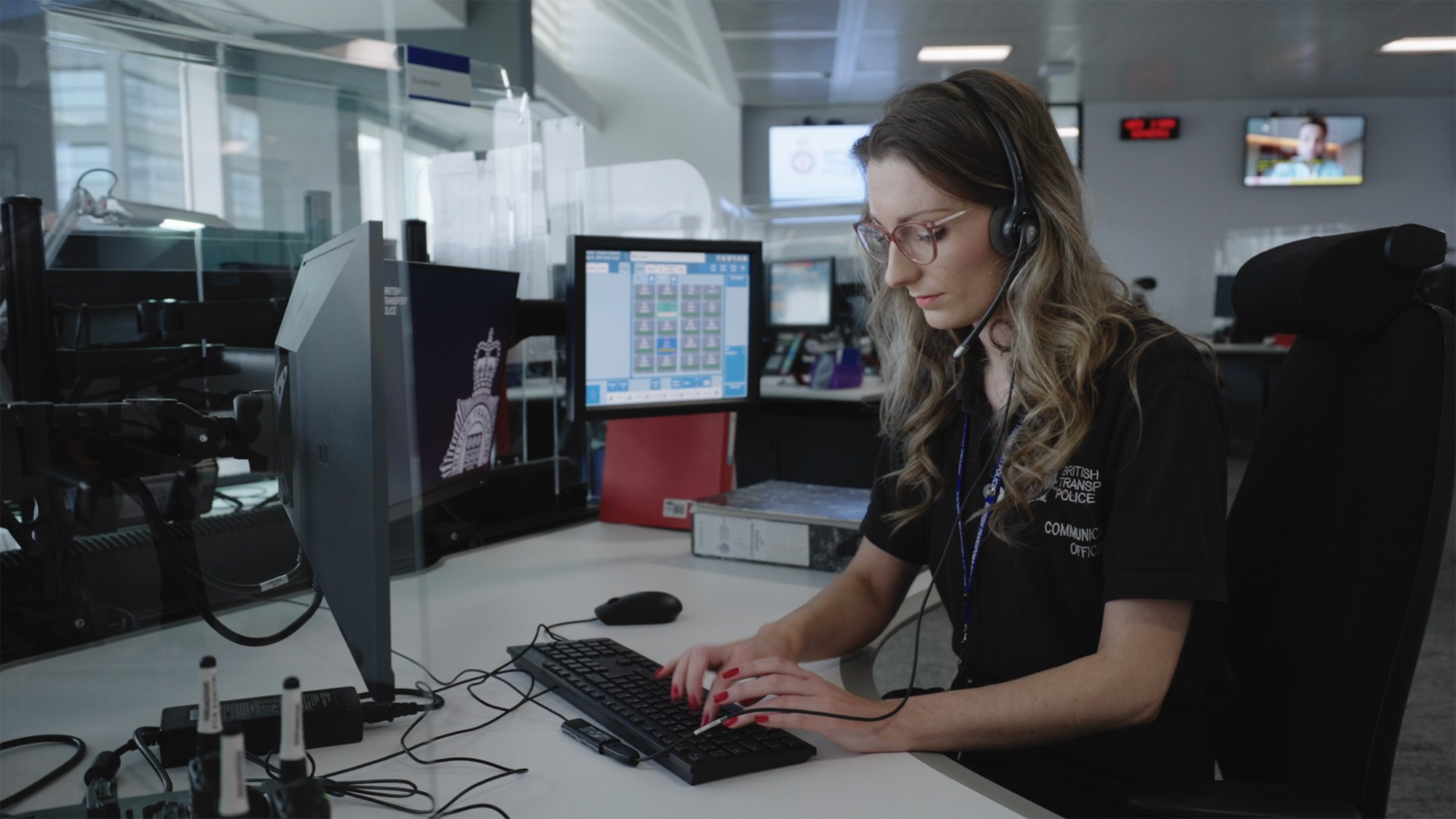 People and culture film production still showing a Communications Officer in a Control Room using a headset and monitoring digital dispatch systems