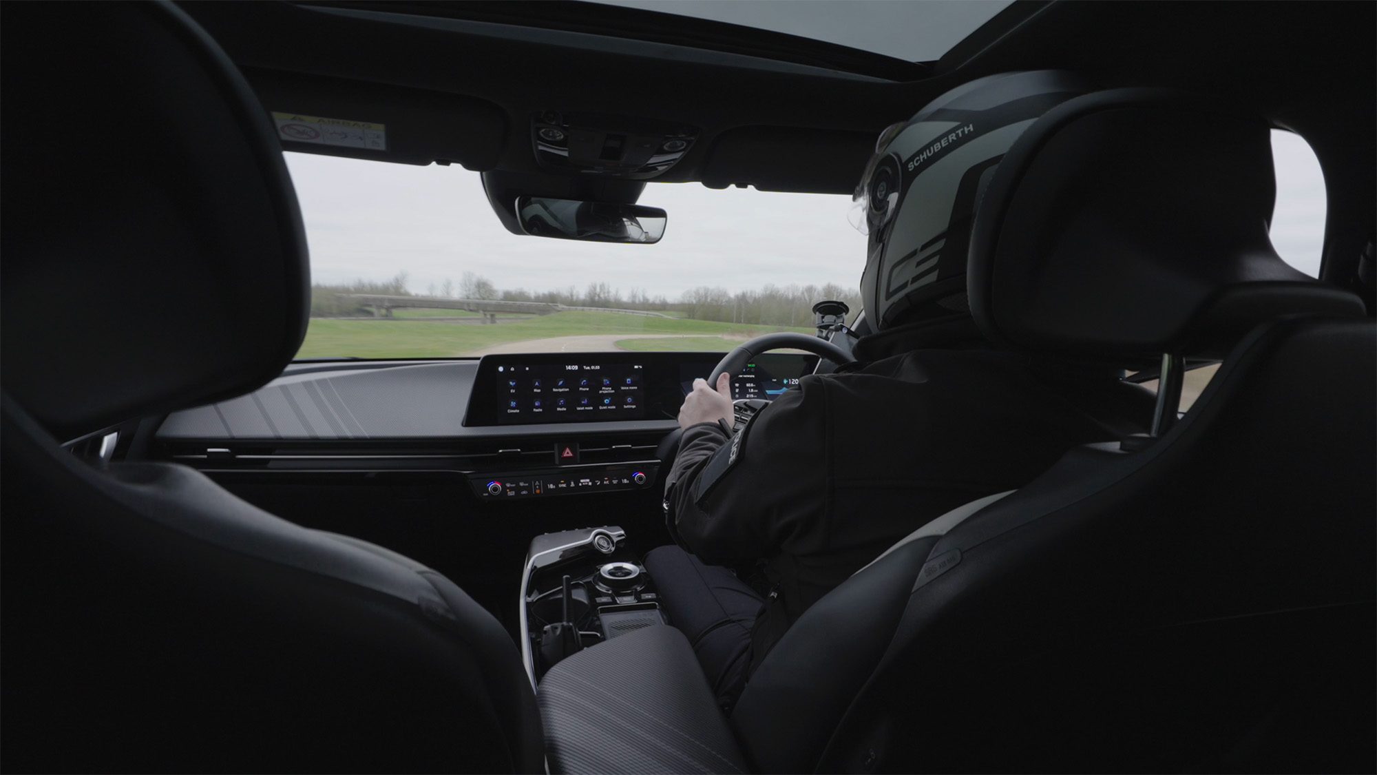 Interior view of a modern car with a helmeted driver and a digital dashboard display during a test drive
