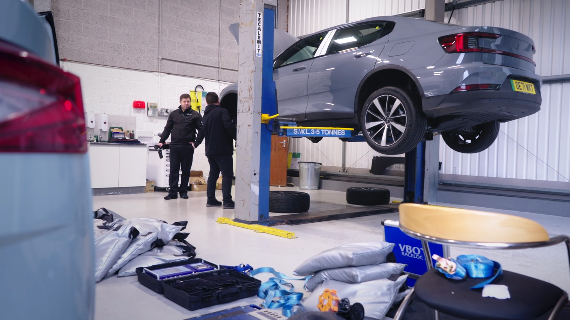 Automotive workshop scene with a car raised on a hydraulic lift and technicians inspecting equipment on the garage floor