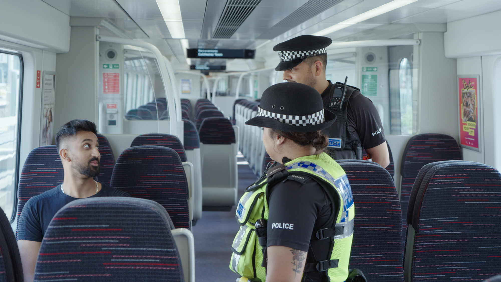 Police officers speaking with a passenger inside a modern train carriage during a routine safety check