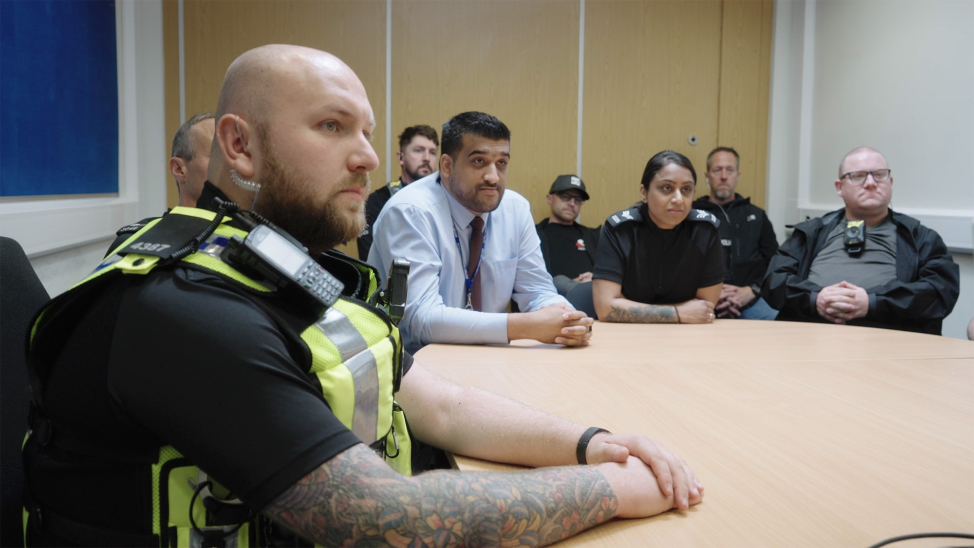 Police officers in high‑visibility vests and staff in business attire seated around a conference table during a professional briefing