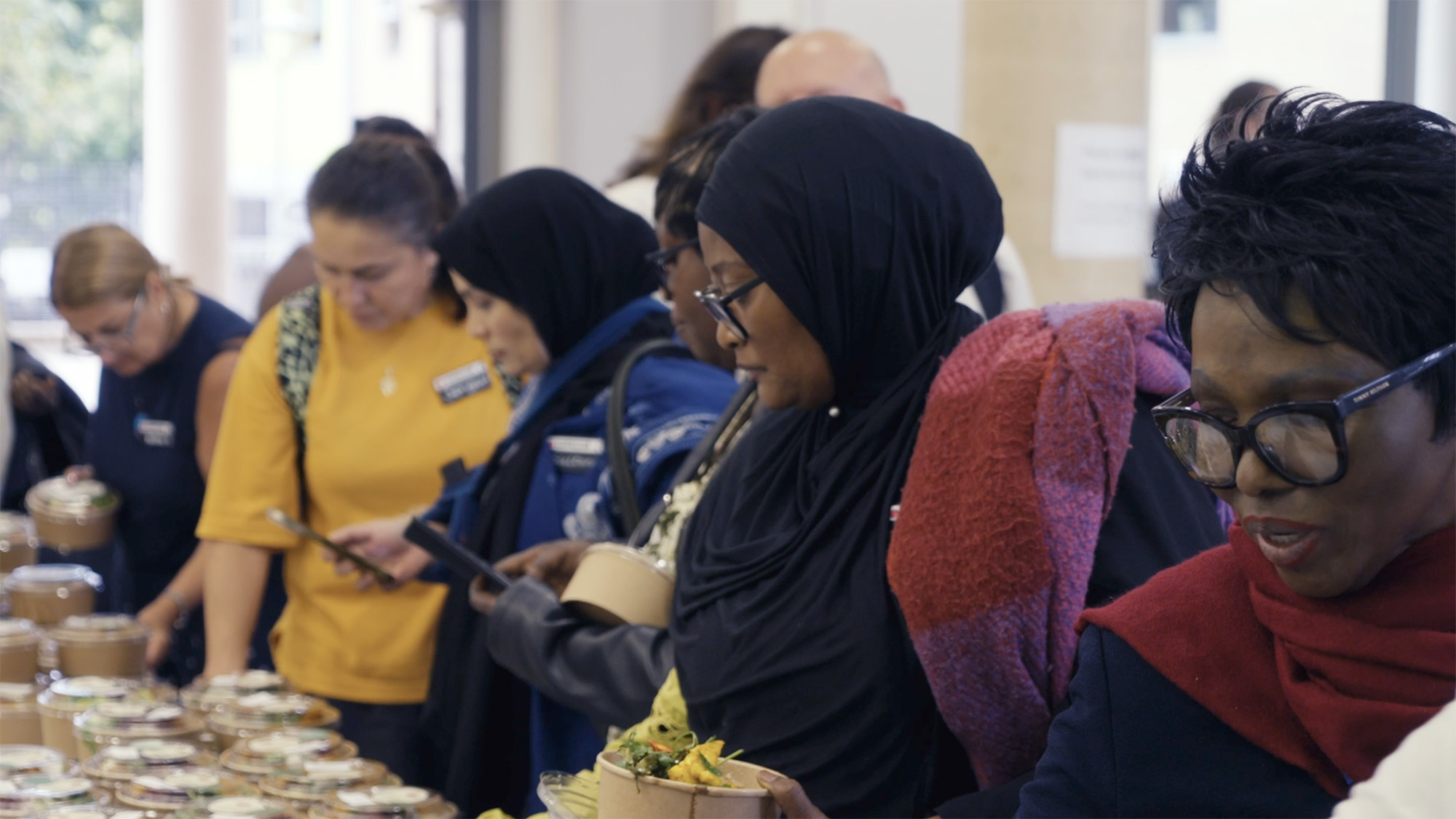 People choosing salads from a table filled with prepared food containers during a community meal event