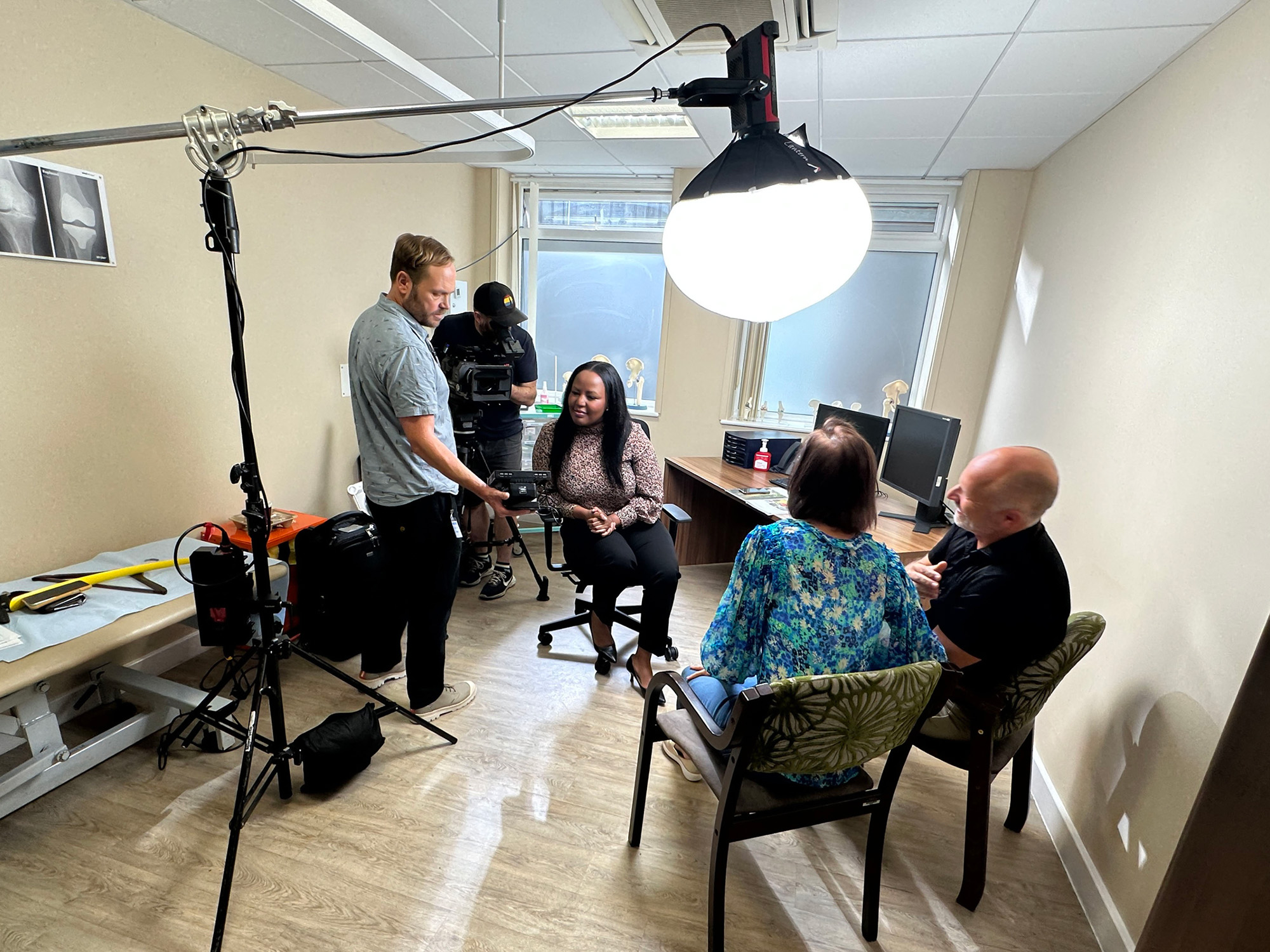 Film crew recording in a medical room with examination equipment and X‑ray images