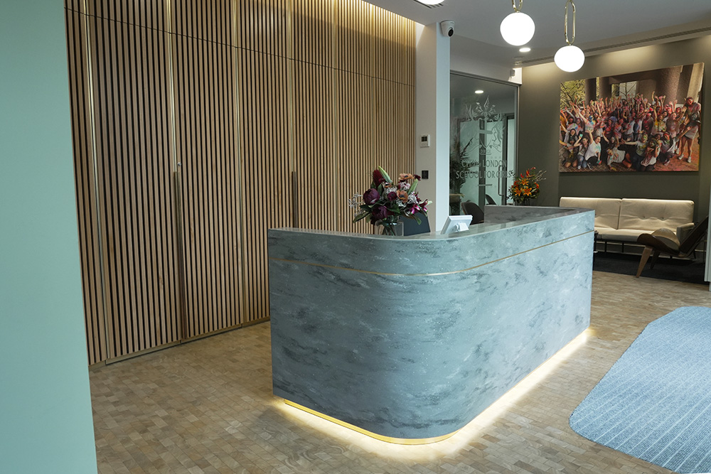 Office reception area featuring a concrete desk, pendant lights and a backdrop of vertical wooden slats