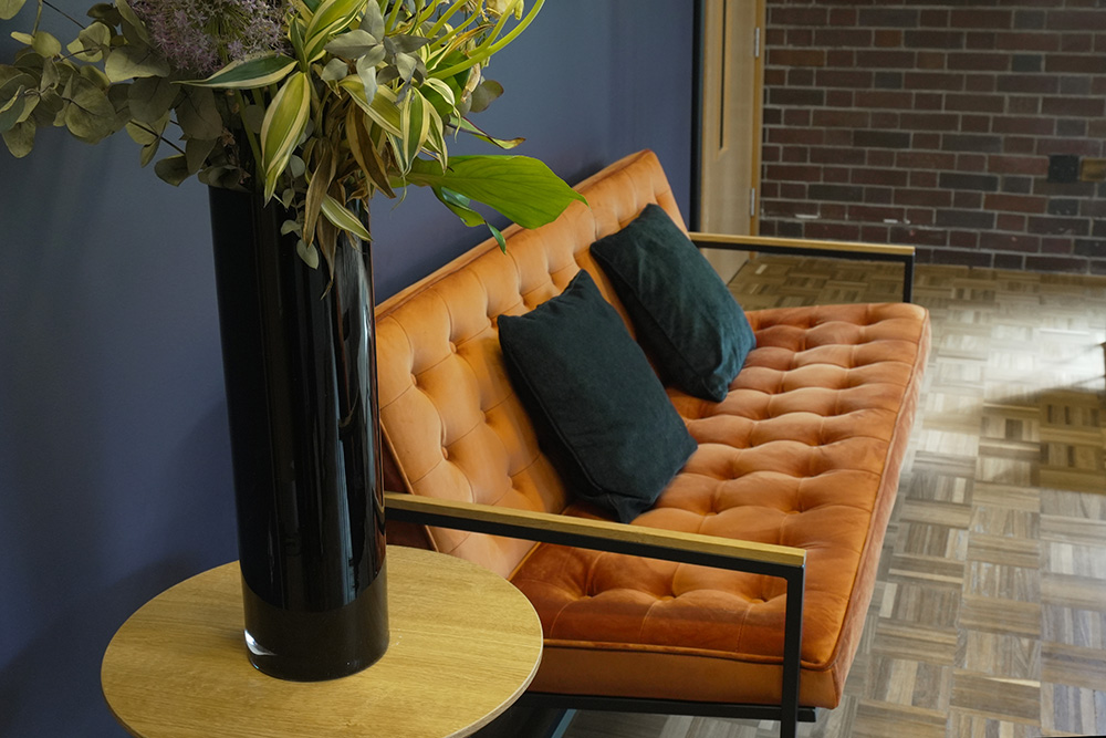 Contemporary seating area with an orange tufted sofa, wooden side table and tall vase of greenery
