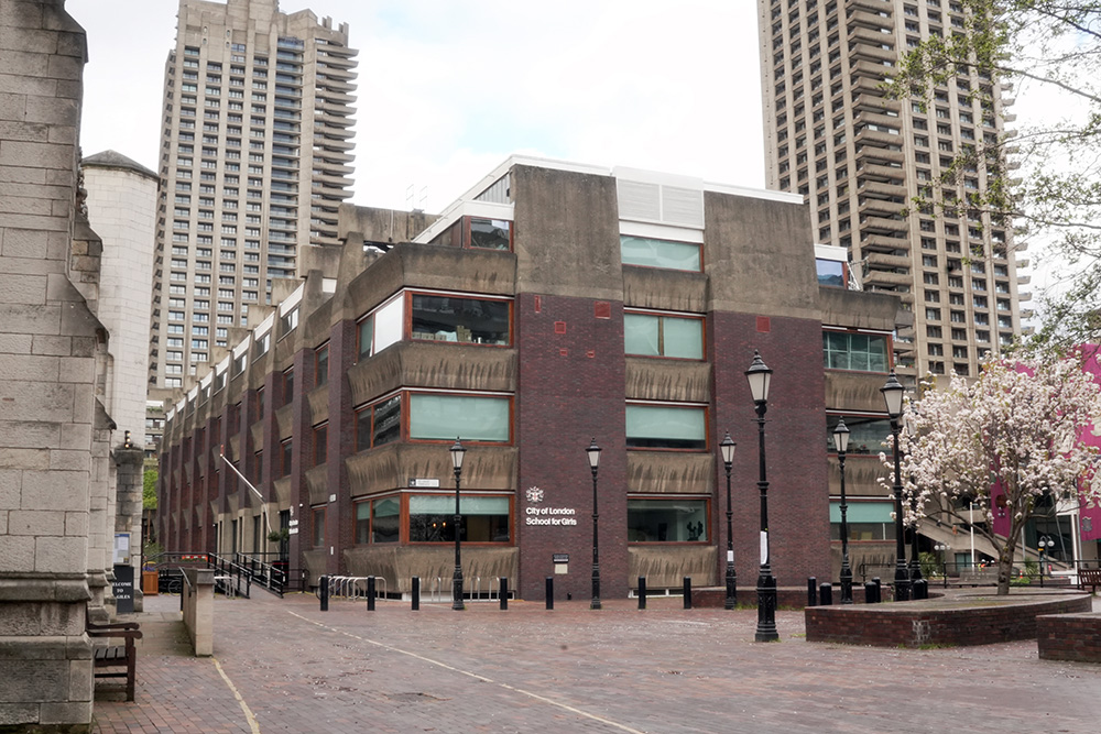 Brutalist concrete and brick exterior of the City of London School for Girls with surrounding Barbican towers and blossoming tree – London architecture