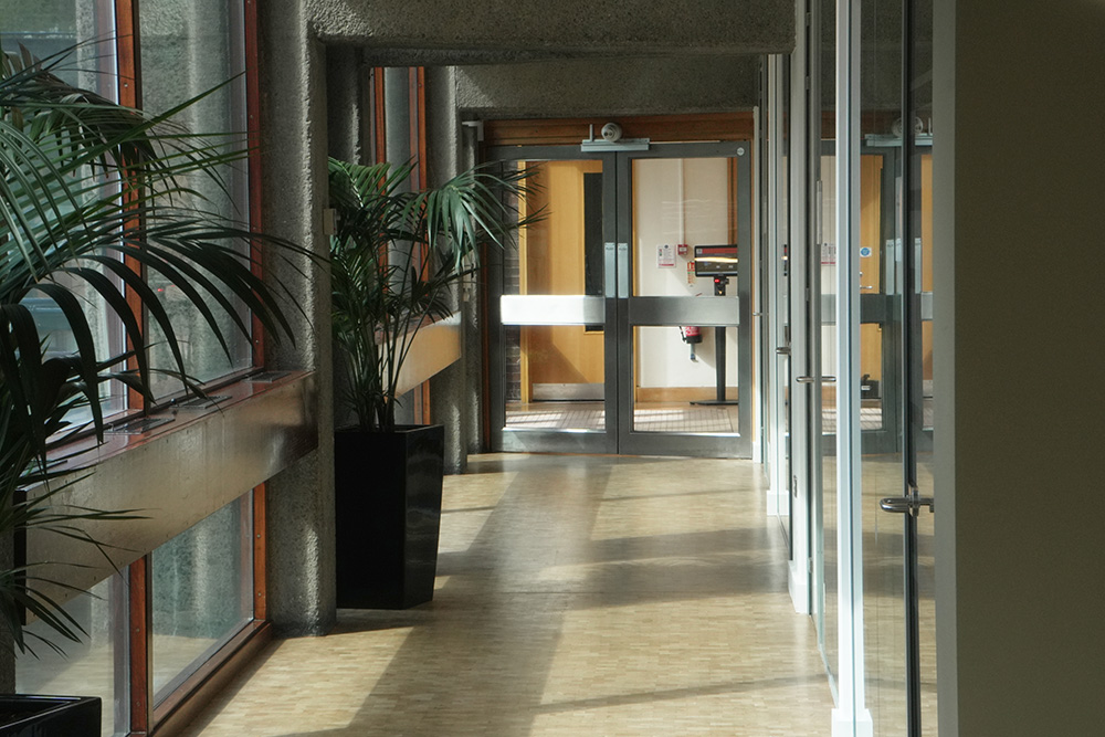 Modern office corridor with wooden chairs, frosted‑glass meeting room and double doors leading to a workspace