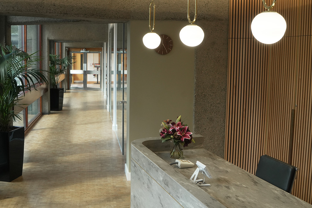 Office reception area featuring a concrete desk, pendant lights and a backdrop of vertical wooden slats