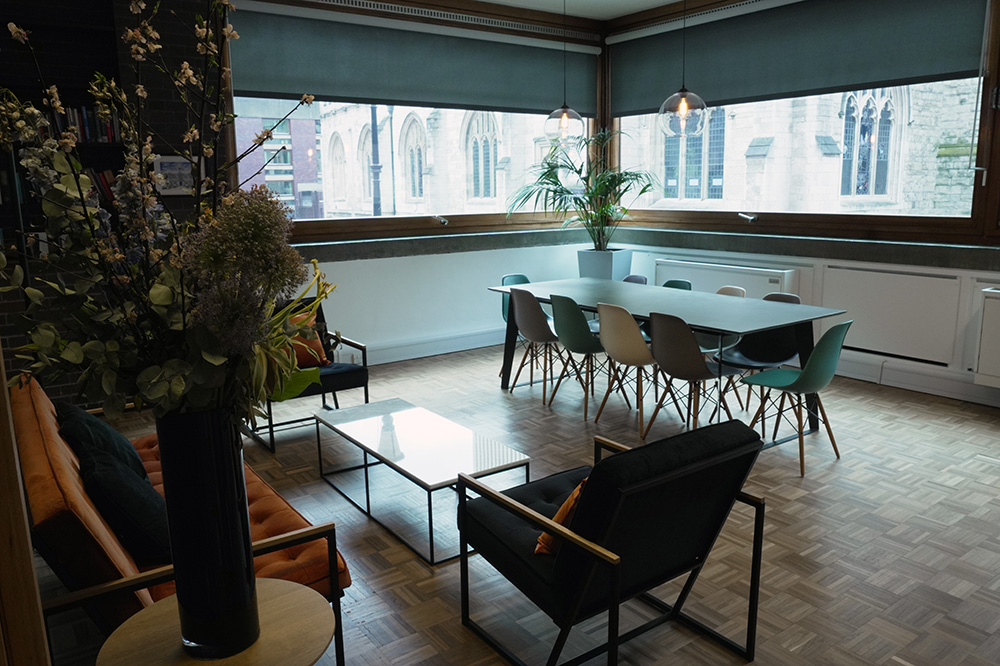 Modern lounge and meeting space with large windows, orange sofa, armchairs and a long communal table