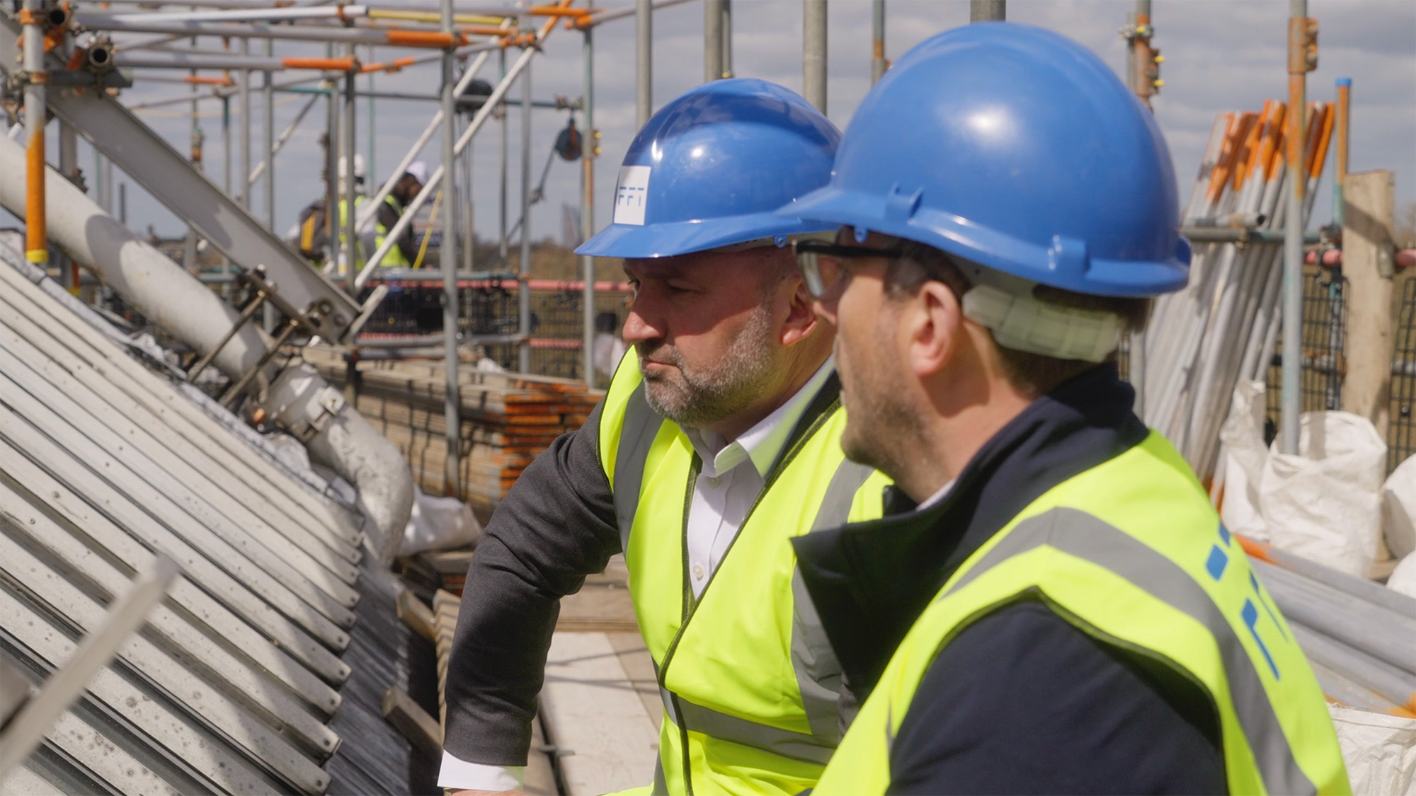 Two workers in safety helmets and high‑visibility vests inspecting metal structures at an active construction site