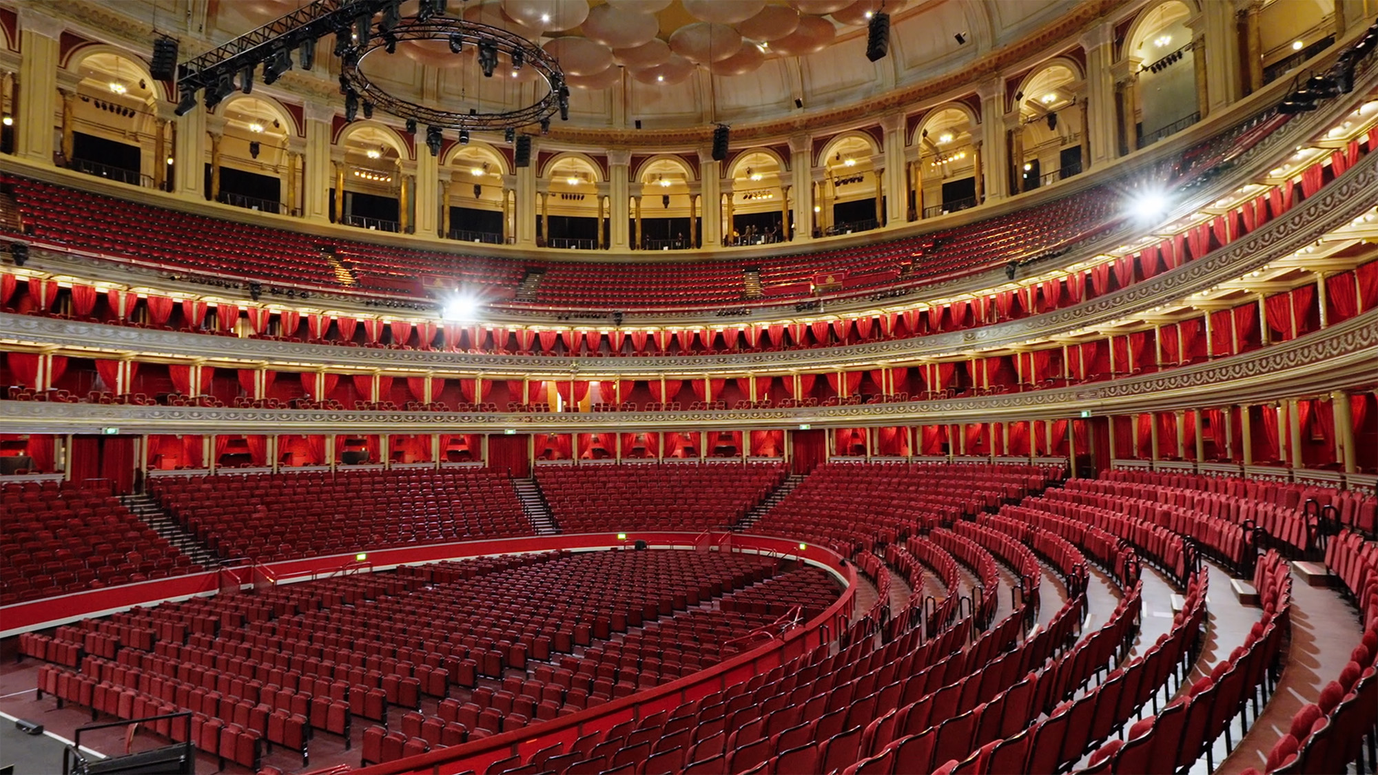 Interior view of the Royal Albert Hall showing red seating, ornate balconies and circular acoustic panels
