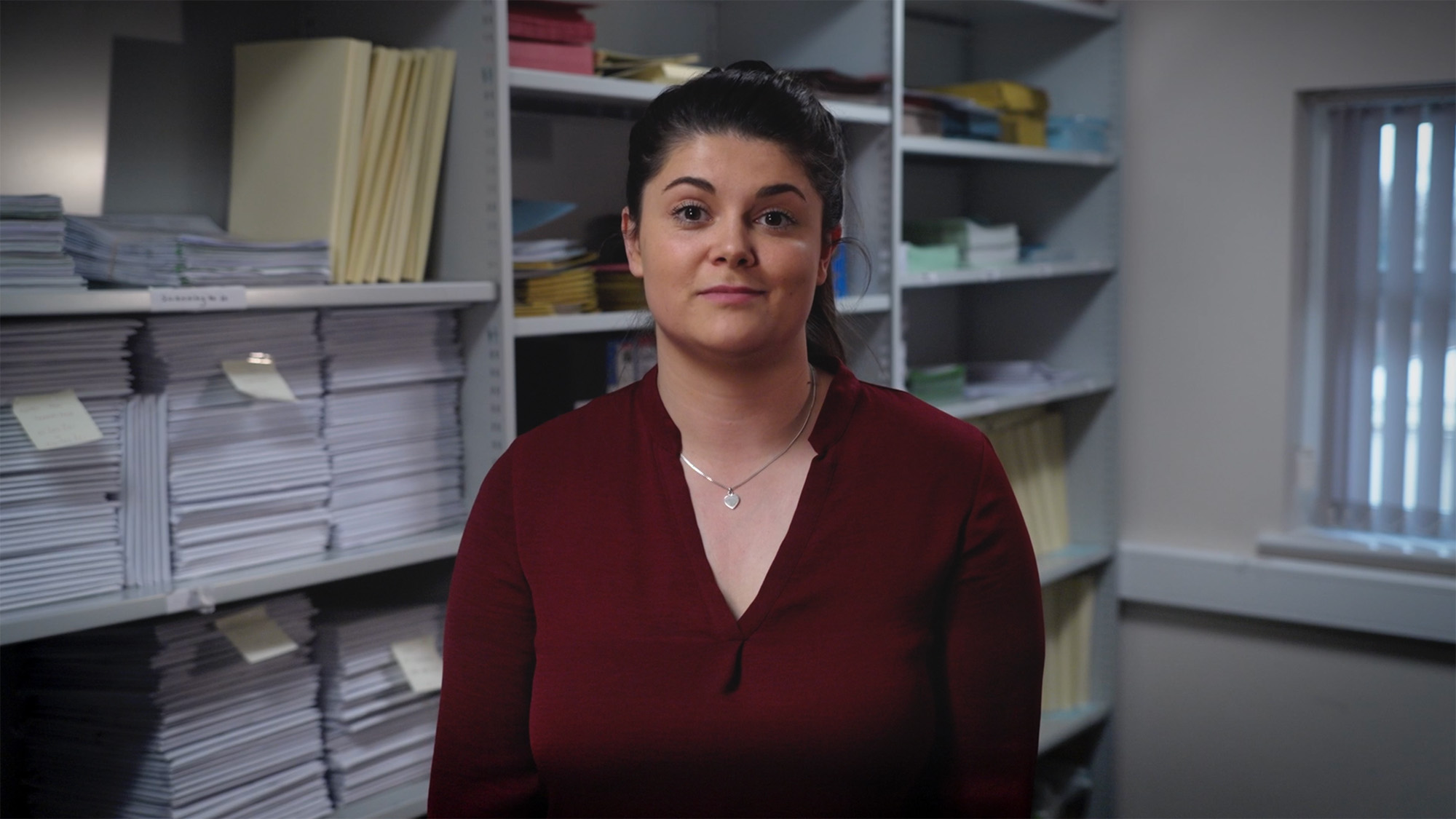 Staff member standing in an office records room with shelves filled with organised stacks of documents and folders