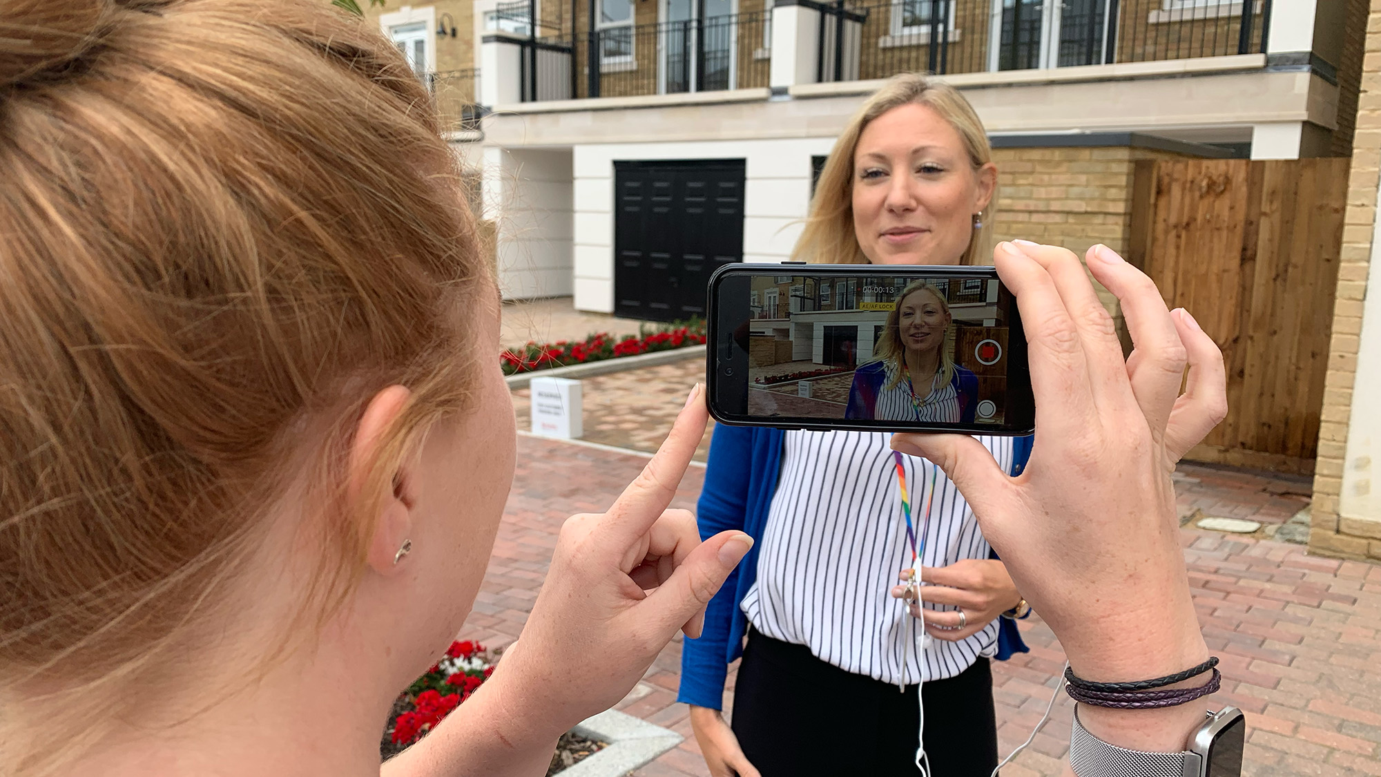 Person holding a smartphone to film someone speaking outside a modern residential building