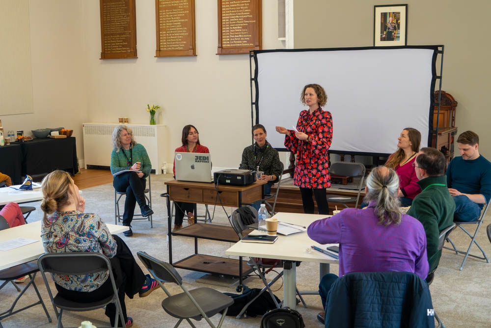Anwen Cooper speaking to a group in a meeting room with a projector and refreshments in the background