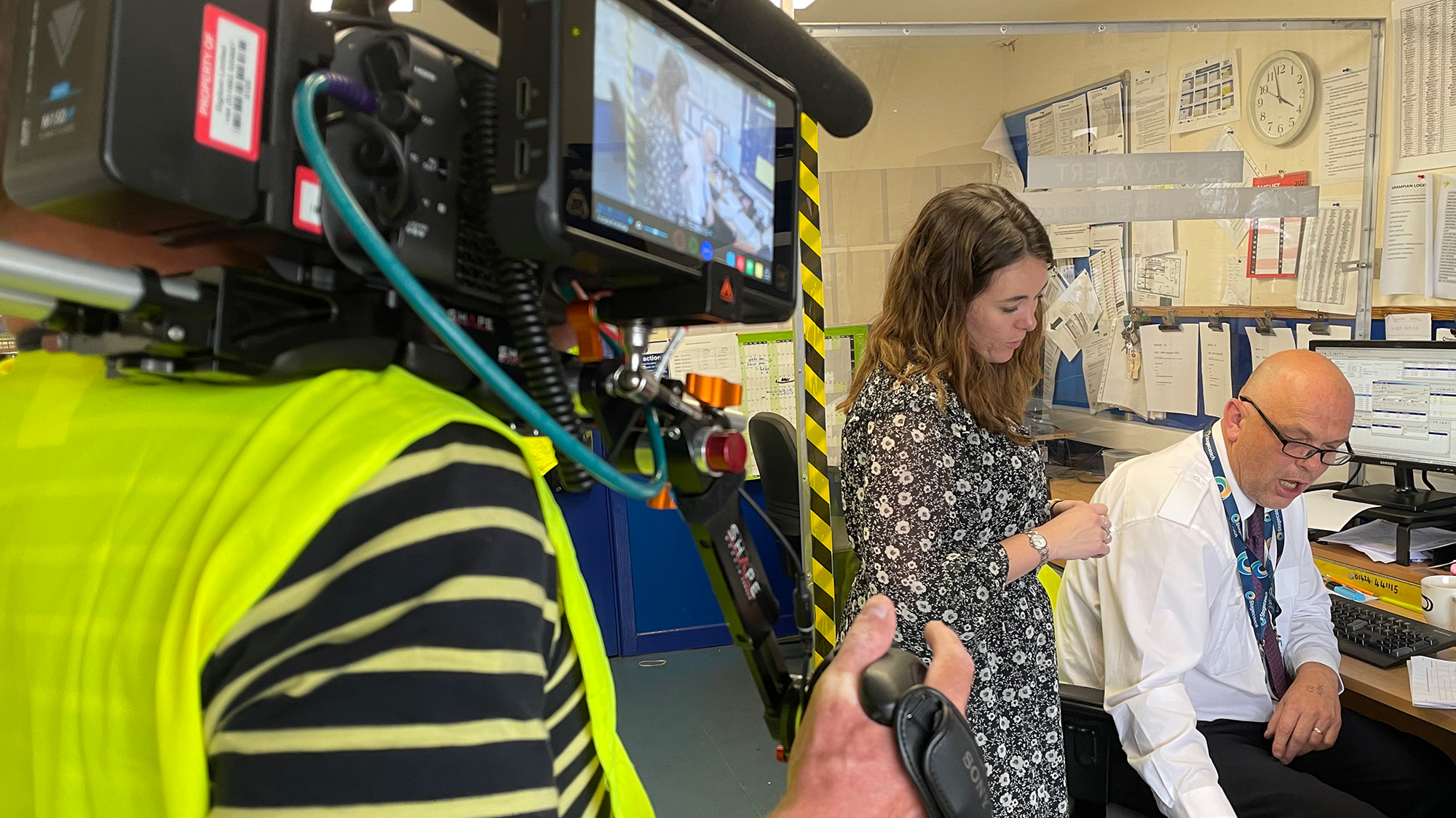 Camera crew filming an office interview with two colleagues discussing work at a desk