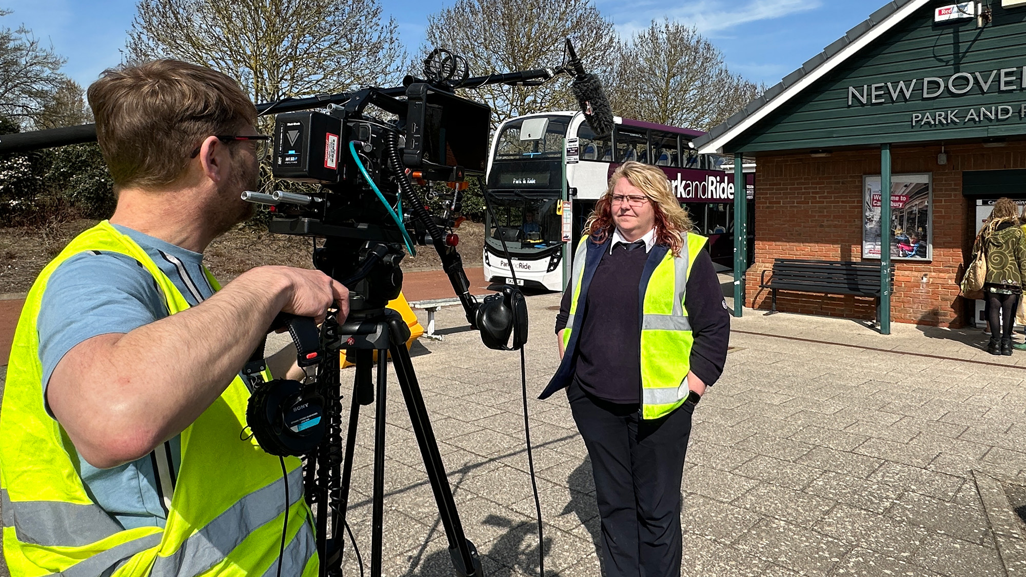 Camera crew filming staff member in high‑visibility vest at Park and Ride bus stop