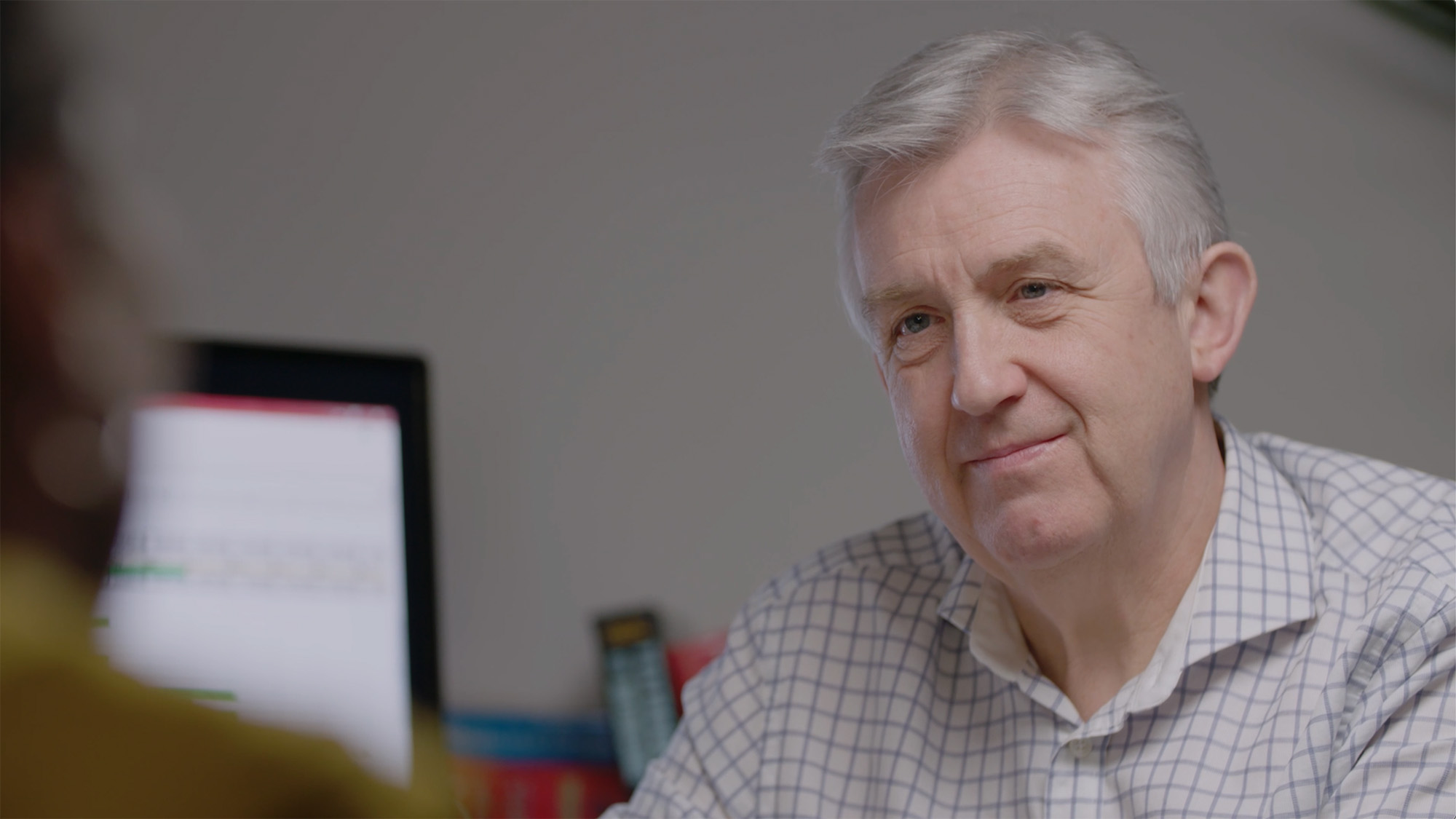 Office-based healthcare education scene for Medthority Learning and Development content, showing an older person near a computer monitor in conversation or focused work