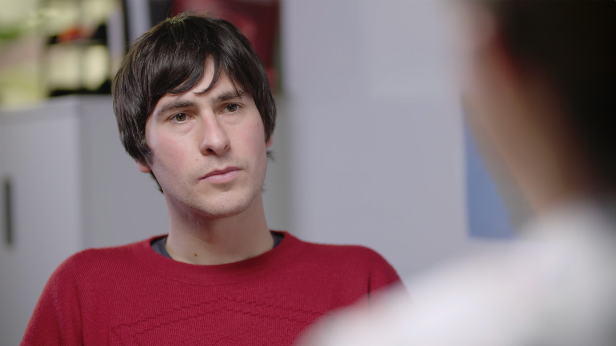 Primary care consultation scene for Medthority smoking cessation training, showing a person in a red sweater seated indoors in conversation