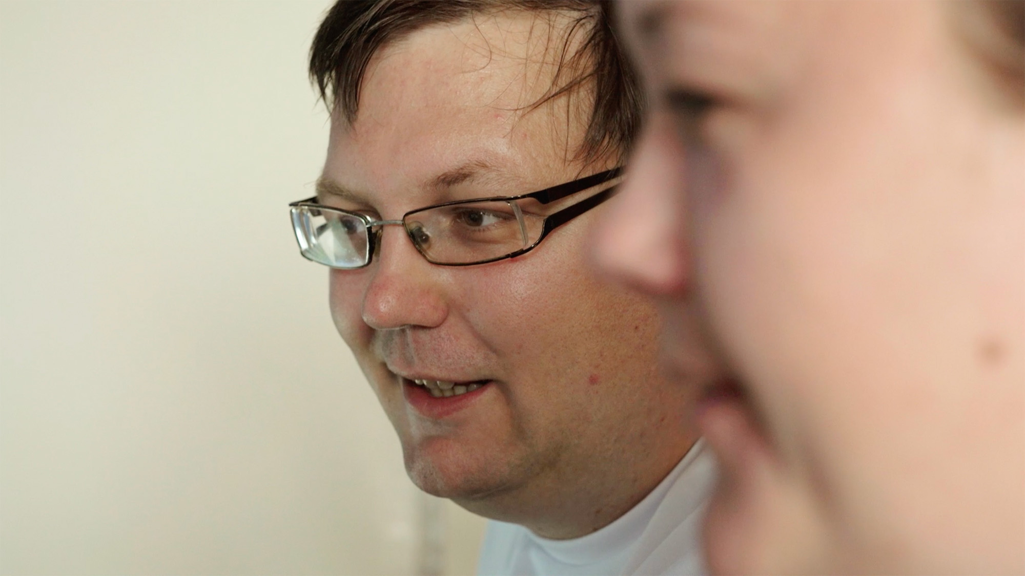 Person wearing glasses engaged in conversation with another individual blurred in the foreground
