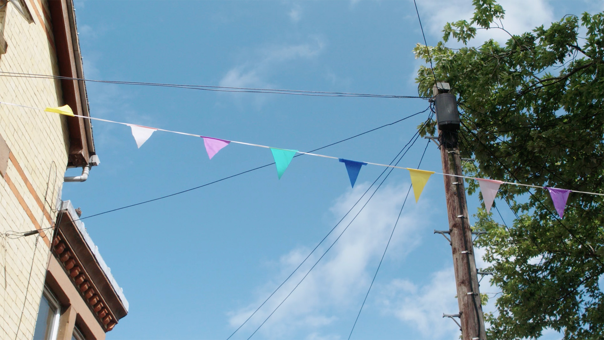 A sunny street scene looking up to a blue sky with multicoloured triangles of flags hanging across the road