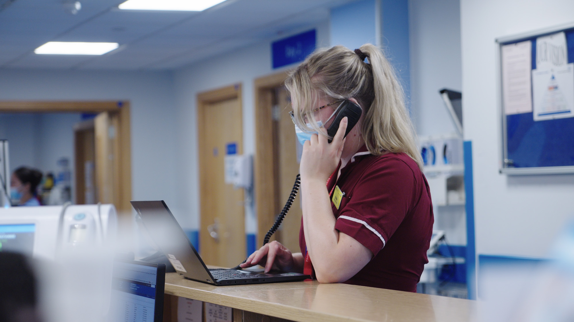 NHS healthcare worker talking on a phone at a nurses station
