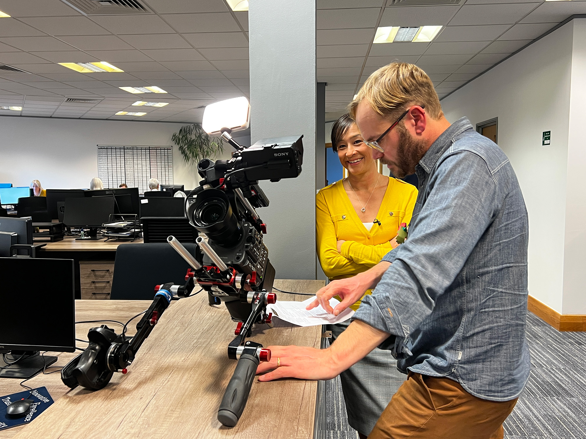 A camera placed on a table with two people chatting between filming an interview in a busy office workspace