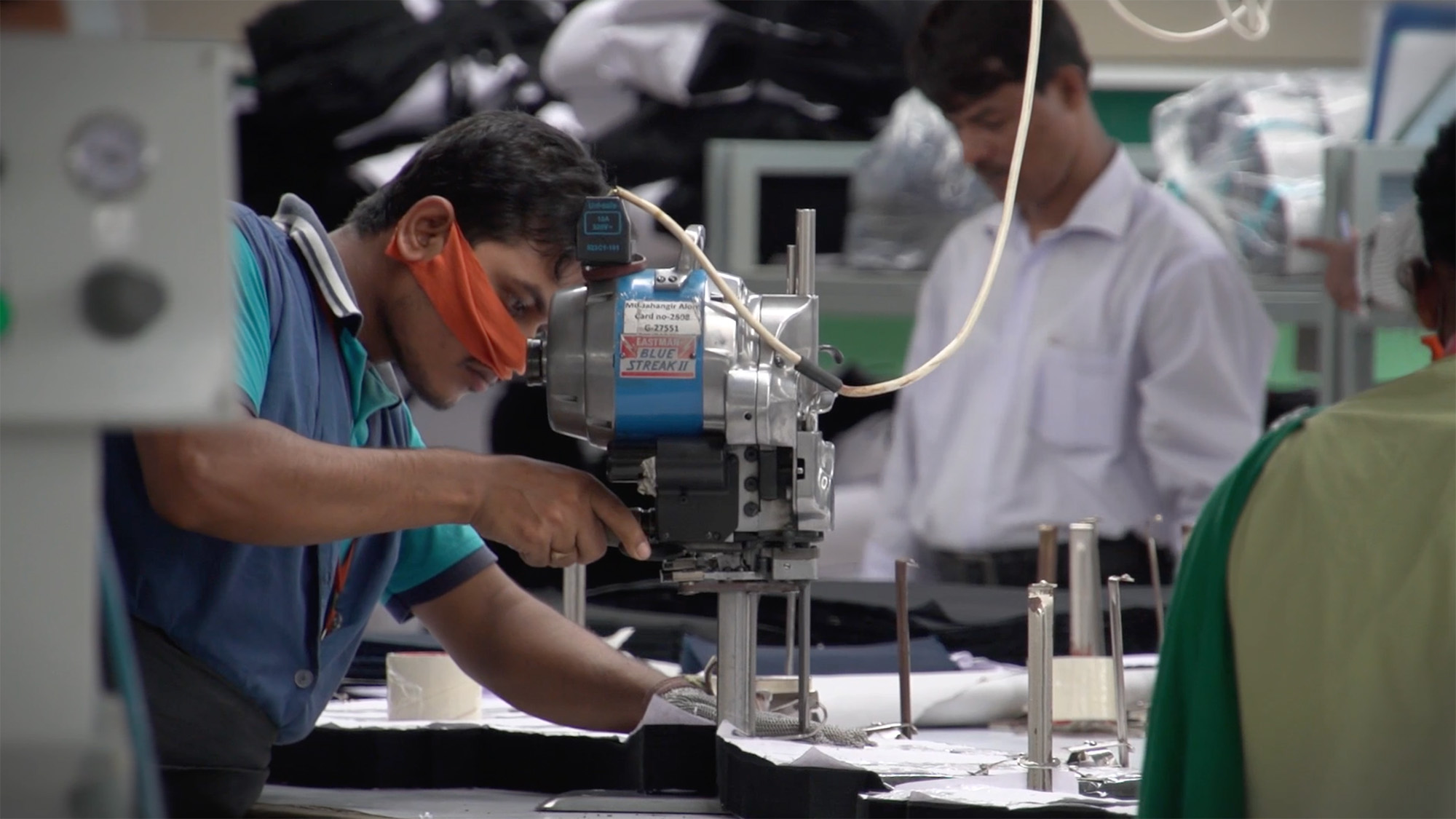 Worker in a mask operating an industrial fabric‑cutting machine in a garment production facility