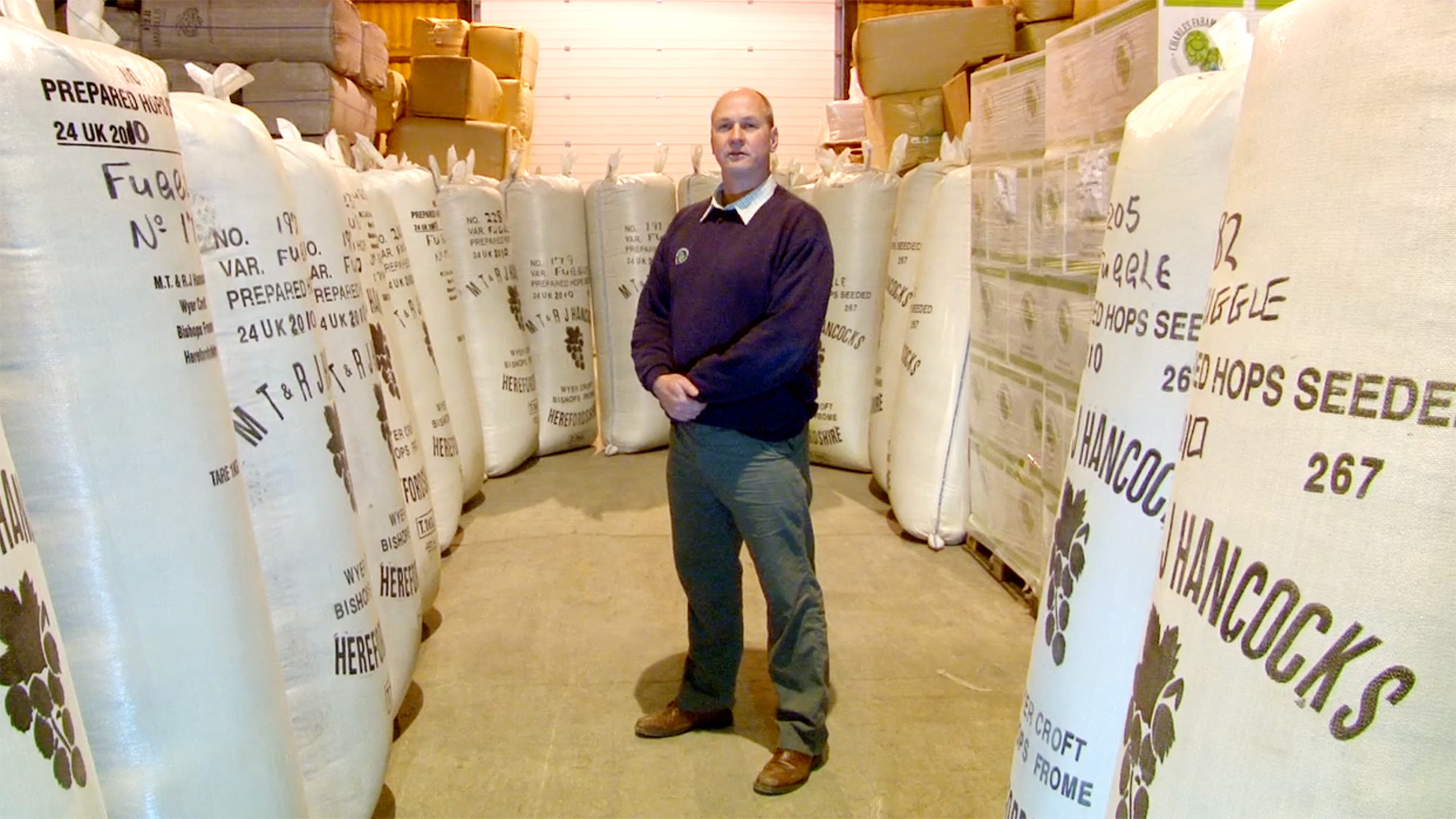 Person standing among rows of large labelled hop sacks in a warehouse