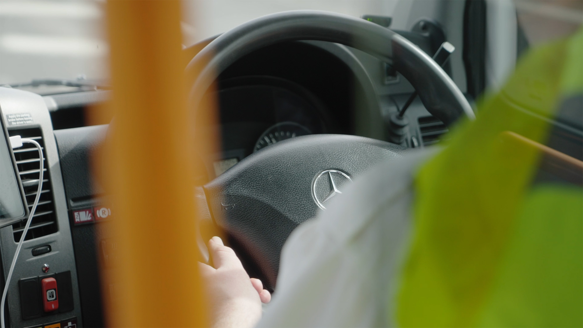 Driver operating a Mercedes‑Benz with a high vis jacket on the back of their seat