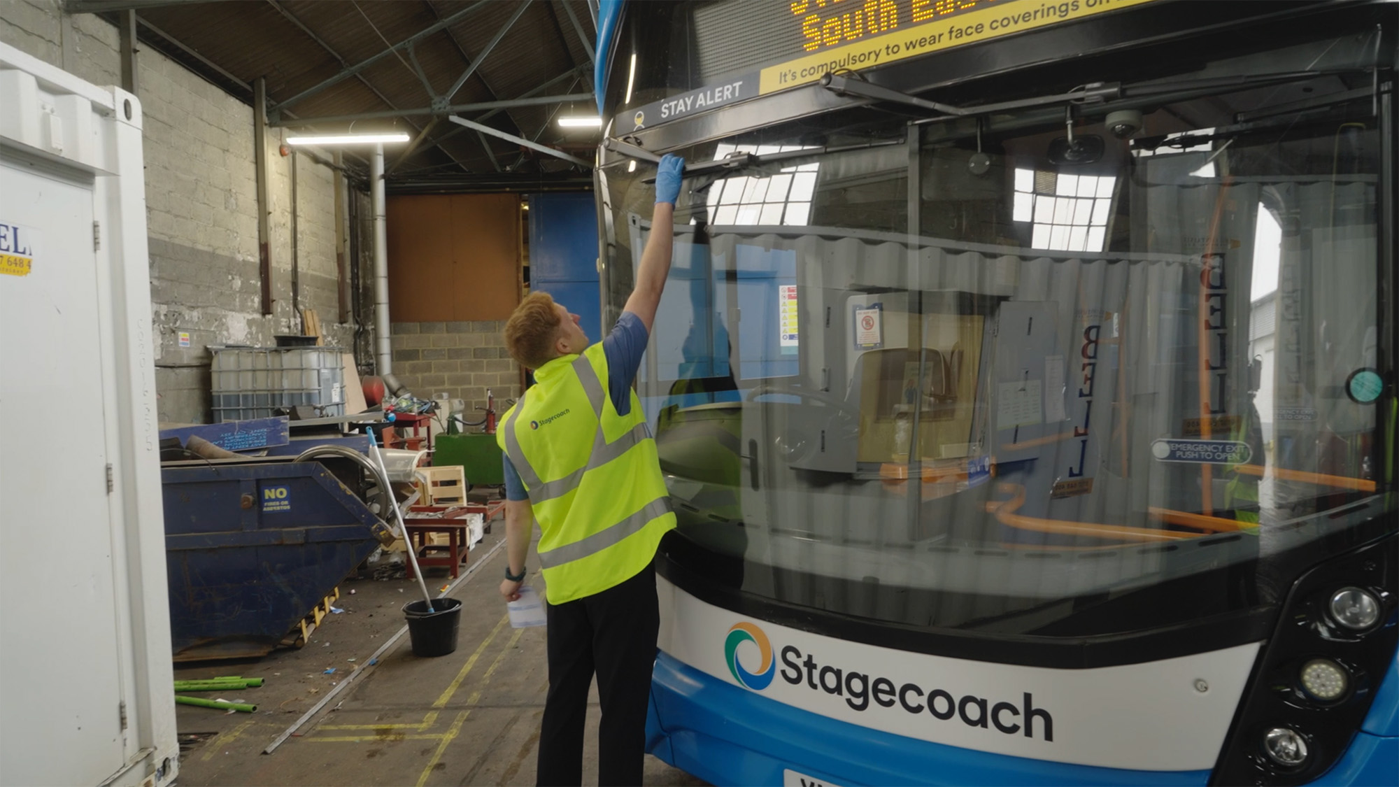 Driver in high‑visibility vest inspecting the front of a Stagecoach bus in a depot
