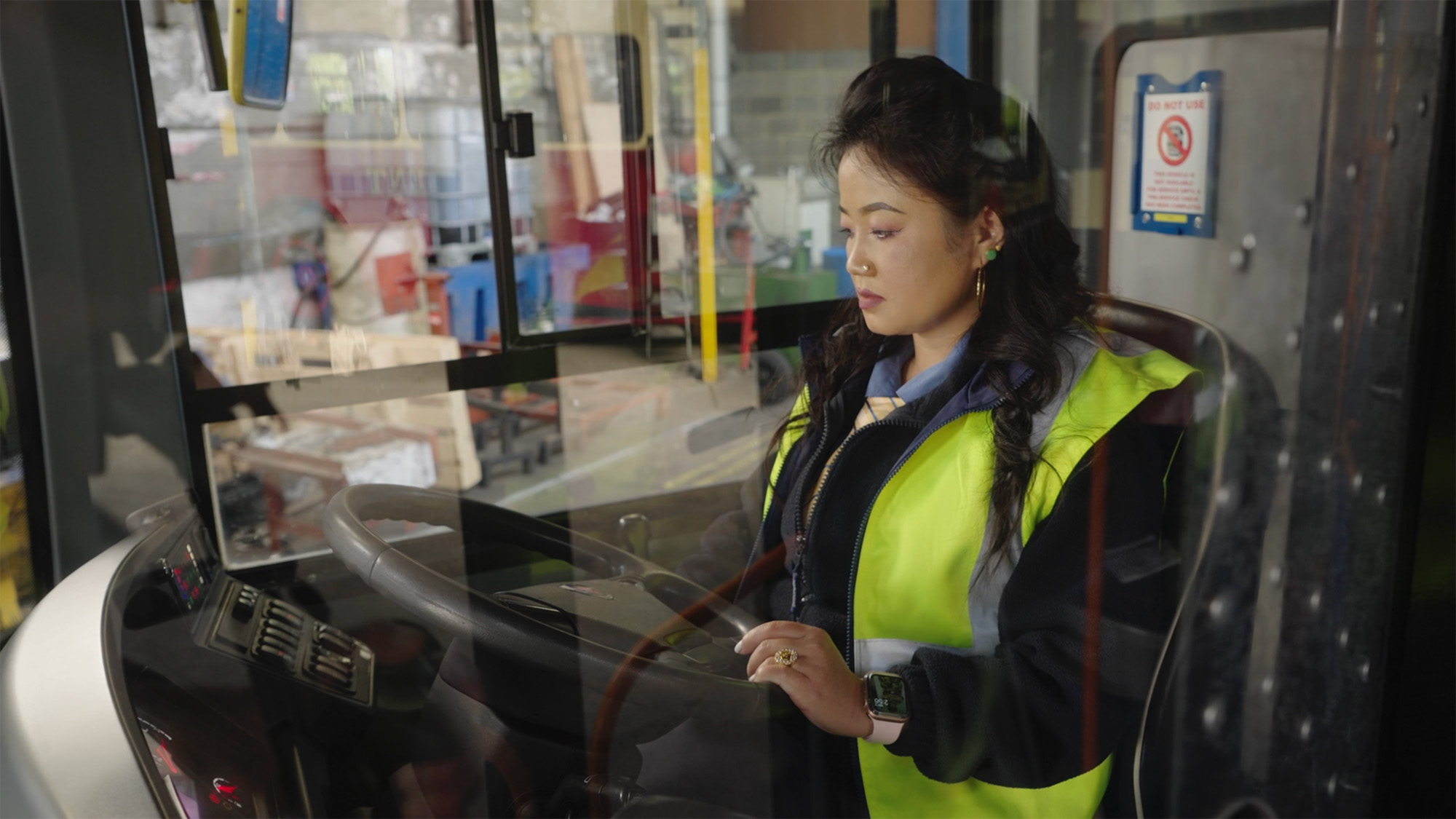 Driver wearing a high‑visibility vest seated inside a vehicle in a maintenance workshop