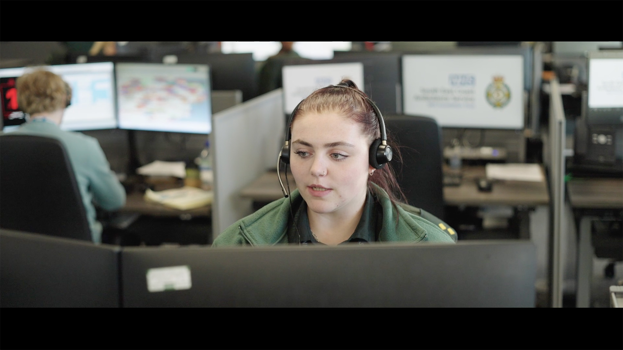 Call handler wearing a headset working at a desk with NHS and ambulance service screens